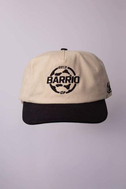 Beige and black cap with 'Barrio' logo on a light gray background